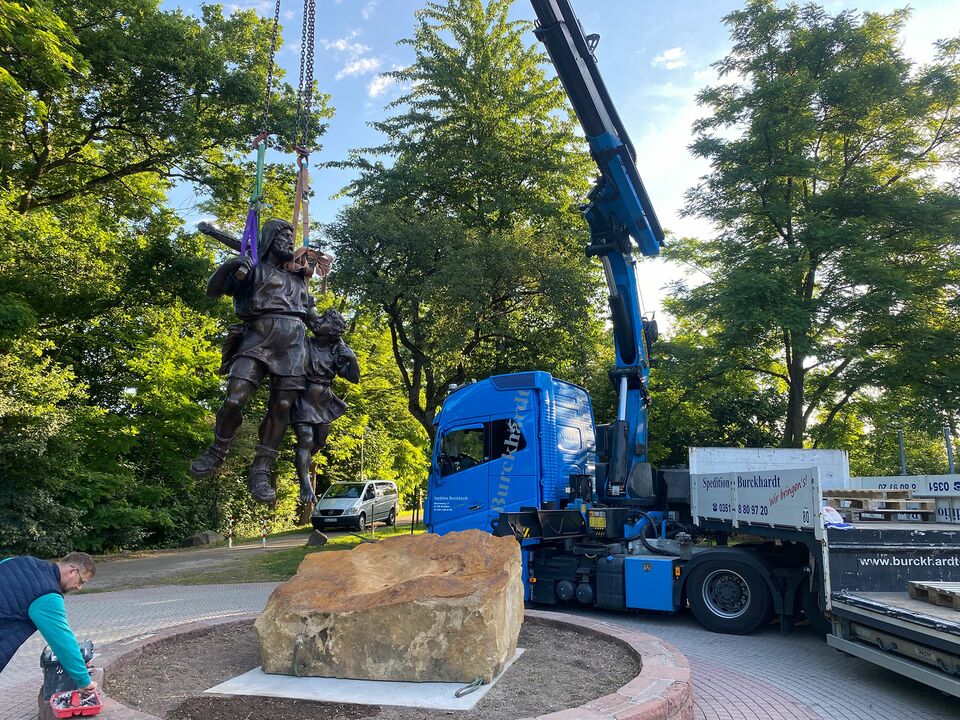 Ein Kran hebt eine große Skulptur in einem Park.