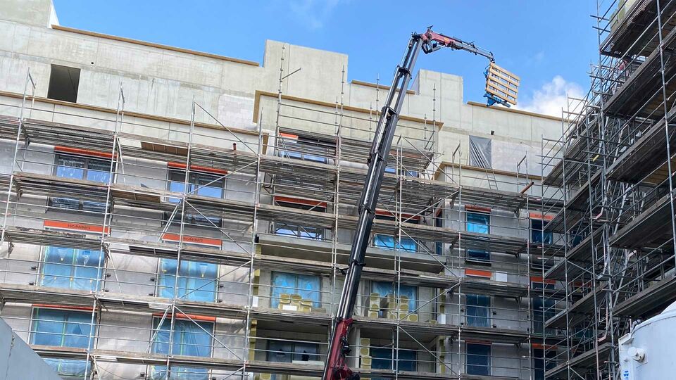 Kranarbeiten auf einer Baustelle mit Gerüst Ein Kran hebt Baumaterialien an einem Gebäude mit Baugerüsten in die Höhe.