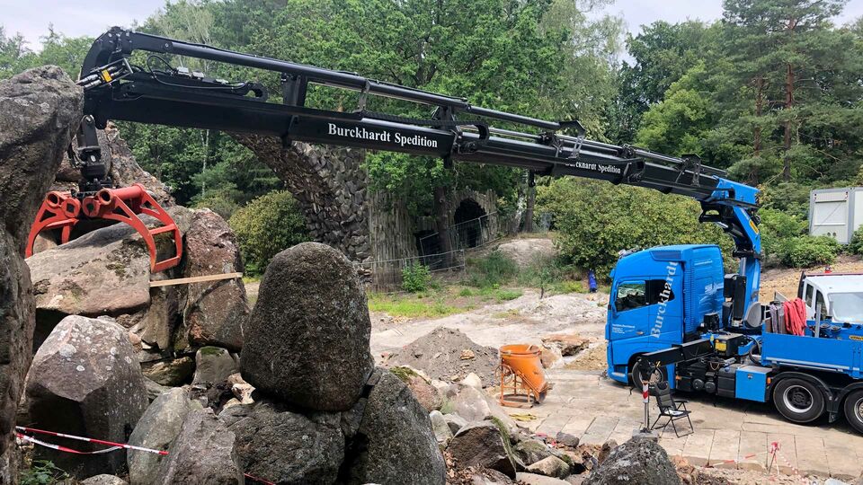 Ein Kran hebt schwere Steine in einem Park.