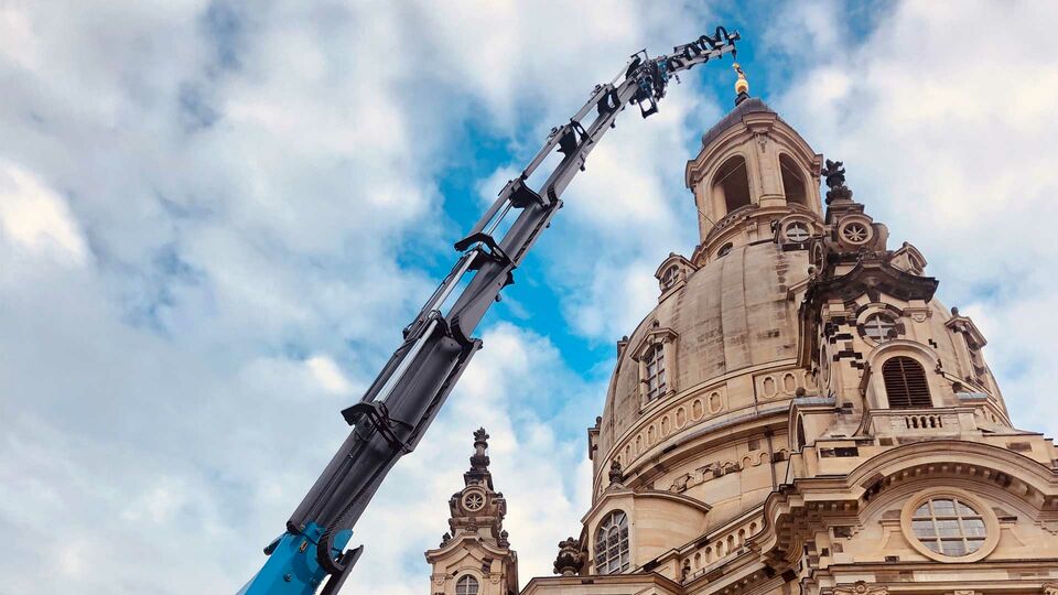 Spezialkran für Arbeiten an historischen Bauwerken Ein großer Kran hebt Bauteile an einem historischen Gebäude, wie einer Kirche, hoch.